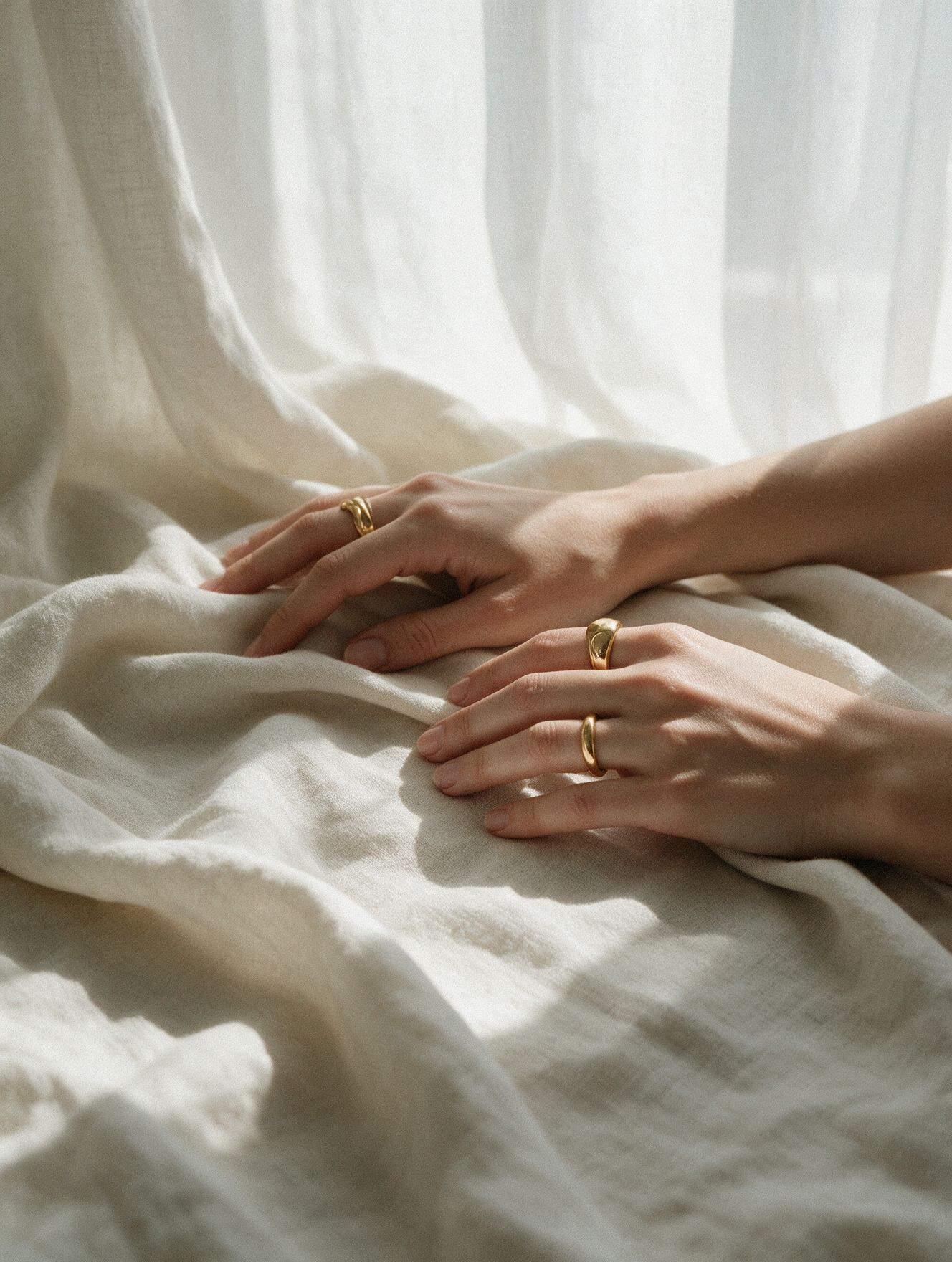 Hands with gold rings resting on ivory fabric